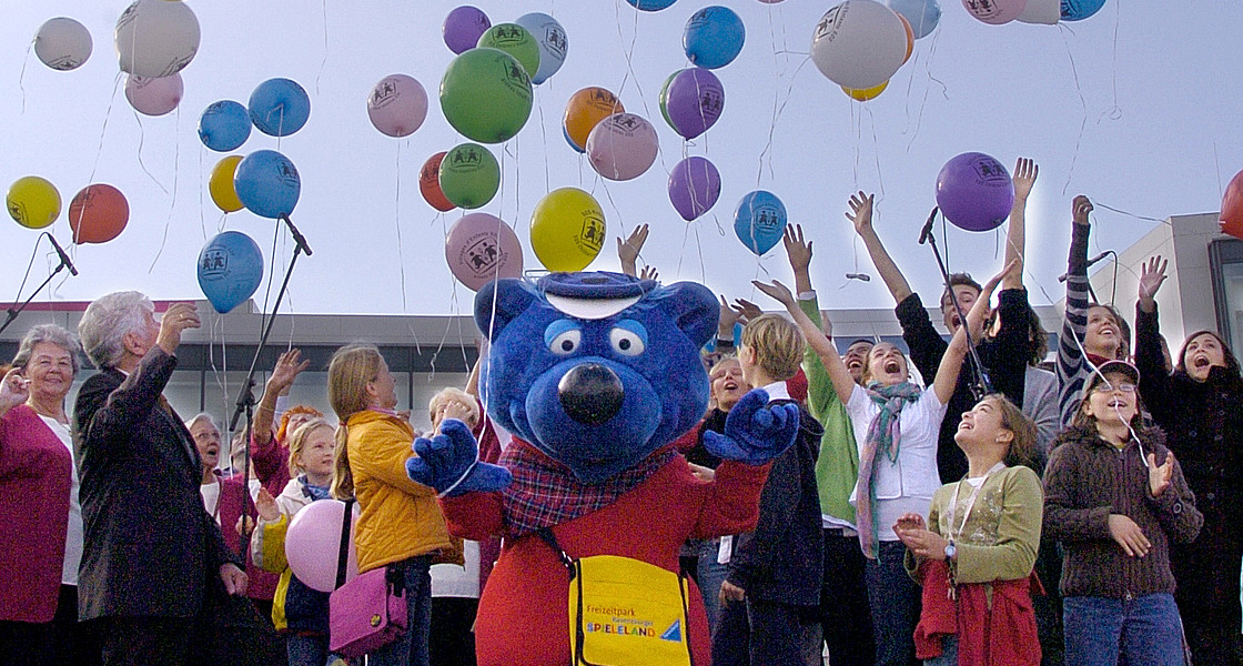Ansicht einer Menschengruppe, mit Luftballons und eine Figur im Kostüm von Käptn Blaubär